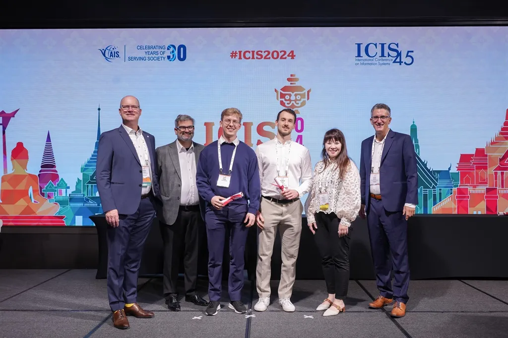 Preisverleihung auf der Bühne der ICIS 2024: sechs Personen, zwei von ihnen halten Urkunden